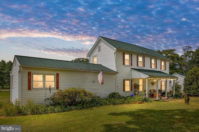 back of property at dusk featuring metal roof, a yard, and a standing seam roof