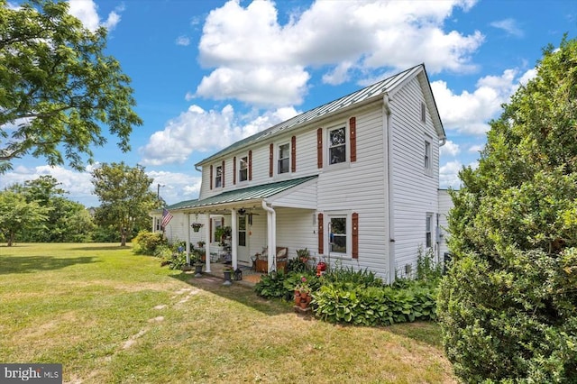 colonial-style house with metal roof, covered porch, a front lawn, and a standing seam roof