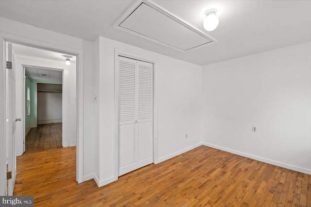 unfurnished bedroom featuring attic access, light wood-style flooring, baseboards, and a closet