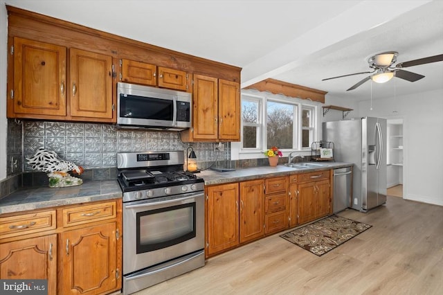 kitchen with a sink, backsplash, stainless steel appliances, brown cabinetry, and ceiling fan