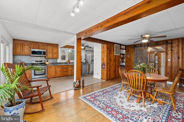 dining space featuring beamed ceiling, wooden walls, ceiling fan, and light wood finished floors