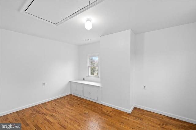 unfurnished room with baseboards, light wood-style floors, and attic access