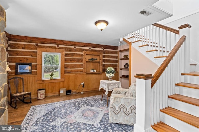 living area with visible vents, wood finished floors, stairs, and wood walls