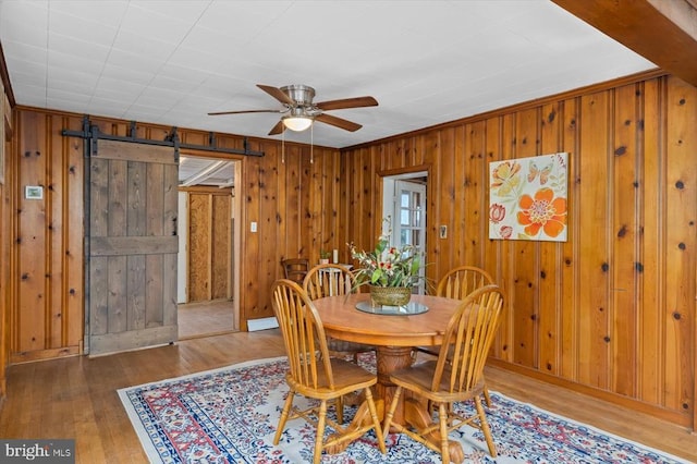 dining space with wooden walls, crown molding, ceiling fan, a barn door, and wood finished floors