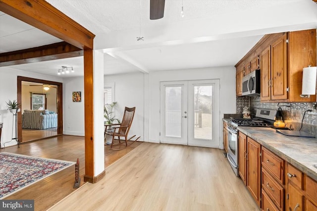 kitchen featuring beam ceiling, light wood-style flooring, a ceiling fan, stainless steel appliances, and decorative backsplash