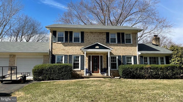 colonial home featuring an attached garage, aphalt driveway, brick siding, a front yard, and a chimney