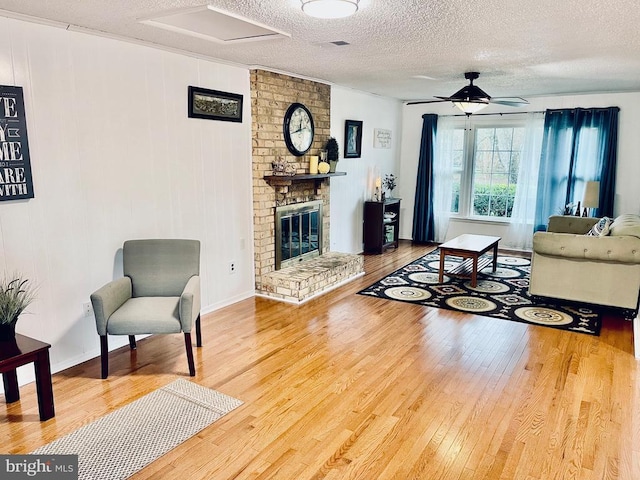 living room with wood finished floors, a fireplace, baseboards, a textured ceiling, and a ceiling fan