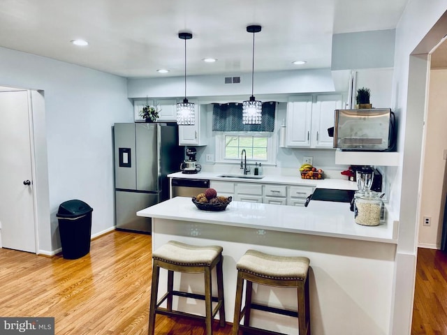 kitchen with a peninsula, stainless steel refrigerator with ice dispenser, light countertops, a sink, and dishwasher