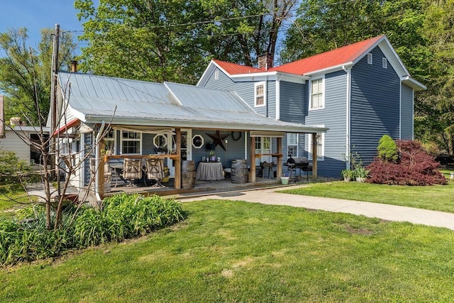 view of front facade featuring covered porch, metal roof, a chimney, and a front lawn