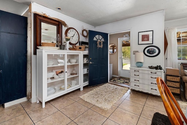 entryway featuring a textured ceiling, baseboards, ornamental molding, and light tile patterned floors