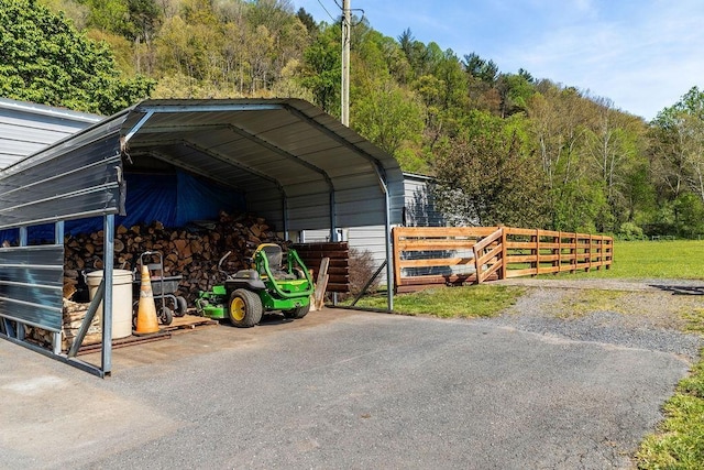view of car parking featuring fence, a wooded view, and a carport