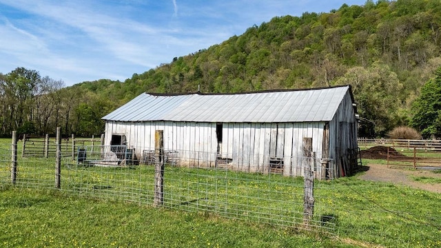 view of pole building featuring a lawn, fence, and a wooded view