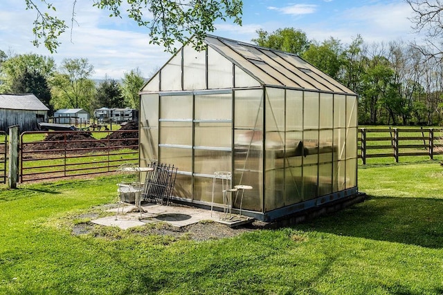 view of greenhouse with fence and a lawn