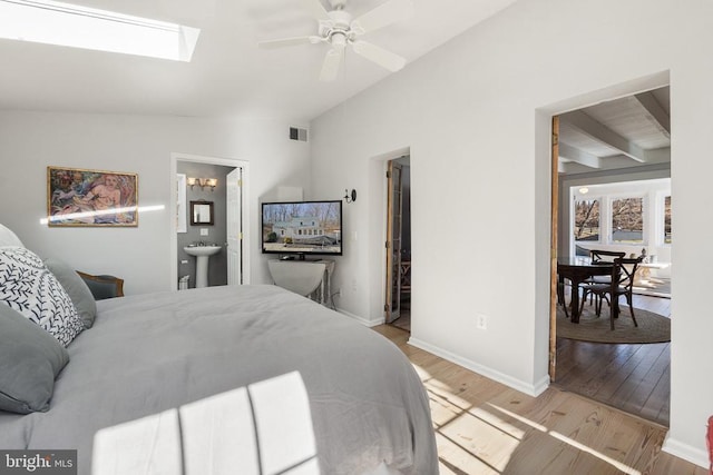 bedroom featuring sink, light hardwood / wood-style floors, connected bathroom, and vaulted ceiling with skylight