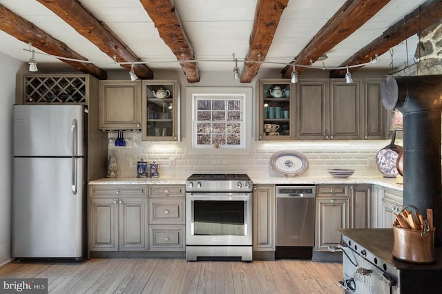 kitchen featuring appliances with stainless steel finishes, light stone counters, light hardwood / wood-style floors, tasteful backsplash, and beam ceiling