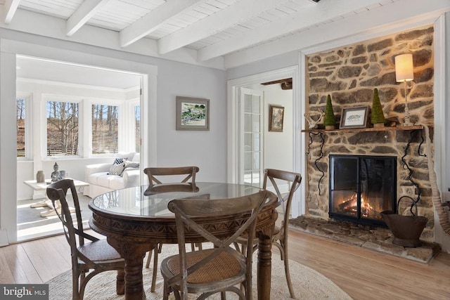 dining room featuring light wood-type flooring, beam ceiling, wooden ceiling, and a fireplace