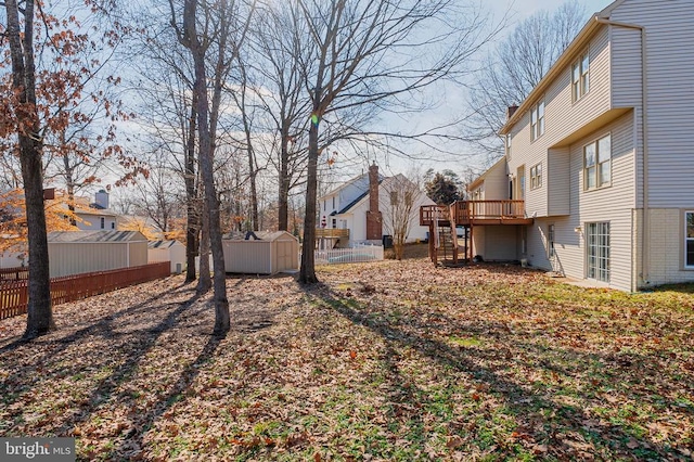 view of yard featuring an outdoor structure, fence, stairway, a wooden deck, and a storage unit