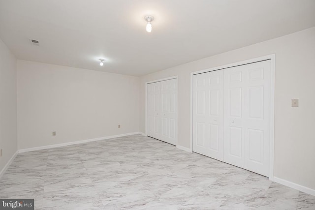 unfurnished bedroom with marble finish floor, baseboards, visible vents, and two closets