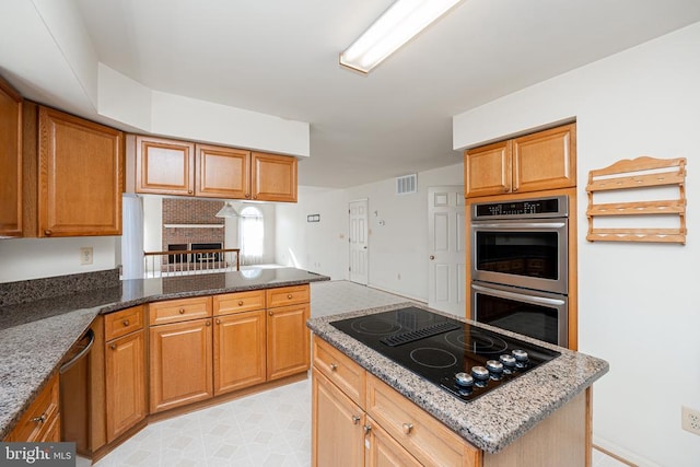 kitchen featuring a center island, a fireplace, appliances with stainless steel finishes, brown cabinetry, and dark stone countertops