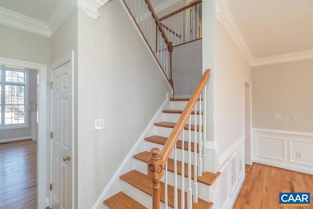 staircase featuring wainscoting, crown molding, a decorative wall, and wood finished floors