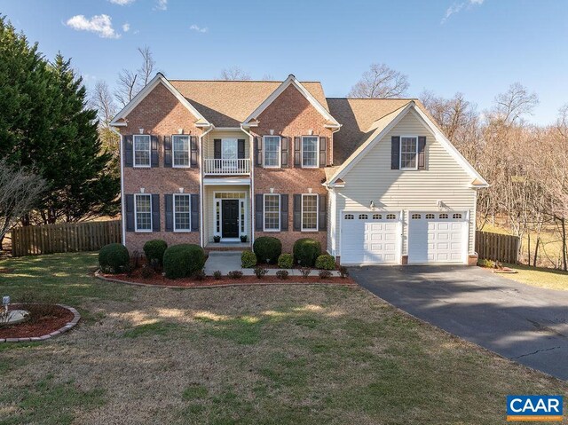 view of front of house featuring a balcony, fence, aphalt driveway, and a front yard