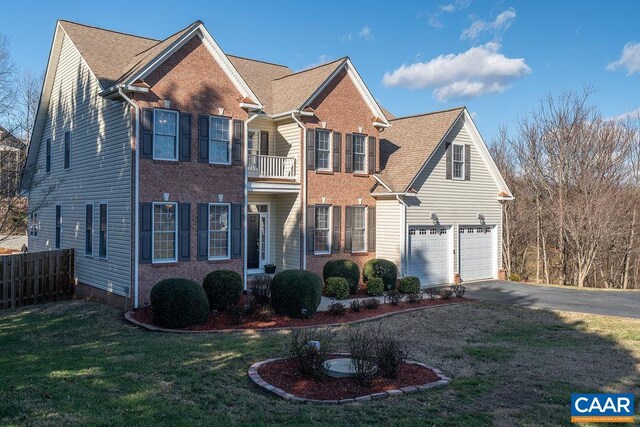 colonial home with brick siding, fence, a balcony, driveway, and a front lawn