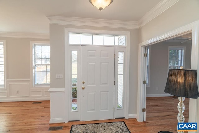 entryway with light wood finished floors, visible vents, and ornamental molding