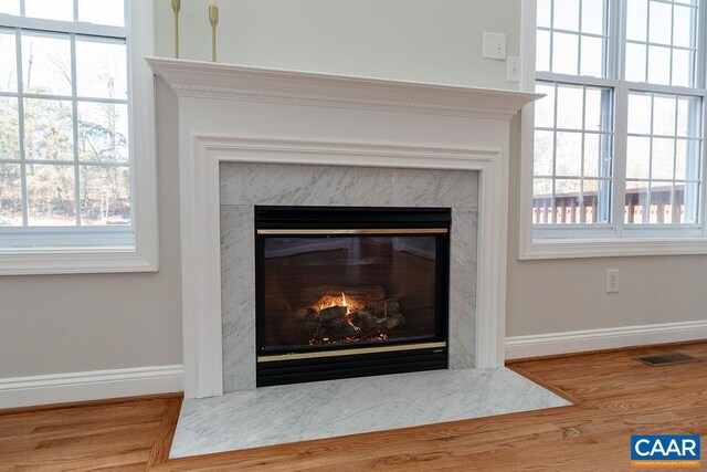 interior details with baseboards, visible vents, wood finished floors, and a high end fireplace