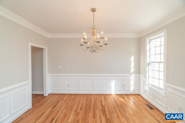 spare room featuring ornamental molding, light wood-type flooring, a chandelier, and visible vents