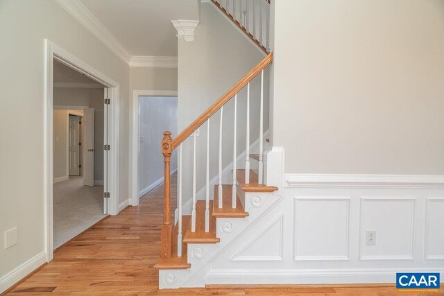 stairway featuring a wainscoted wall, ornamental molding, wood finished floors, and a decorative wall