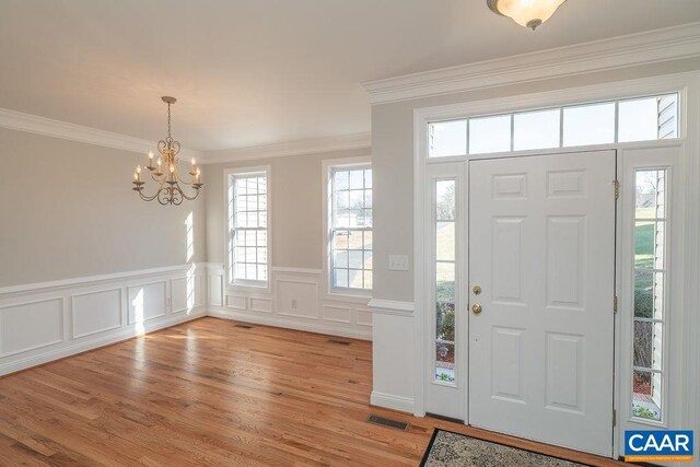 entrance foyer featuring light wood-type flooring, visible vents, crown molding, and an inviting chandelier