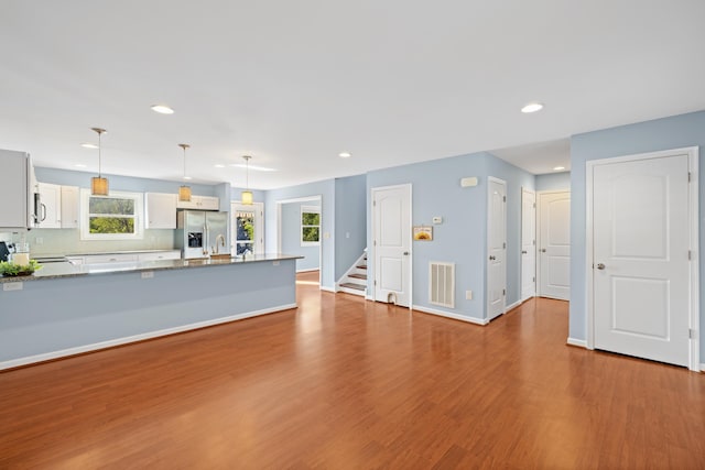 unfurnished living room with stairs, recessed lighting, baseboards, wood finished floors, and visible vents