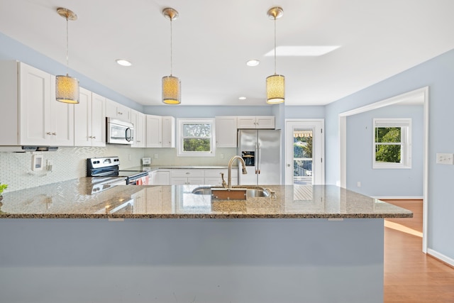 kitchen featuring stone countertops, a sink, appliances with stainless steel finishes, backsplash, and decorative light fixtures