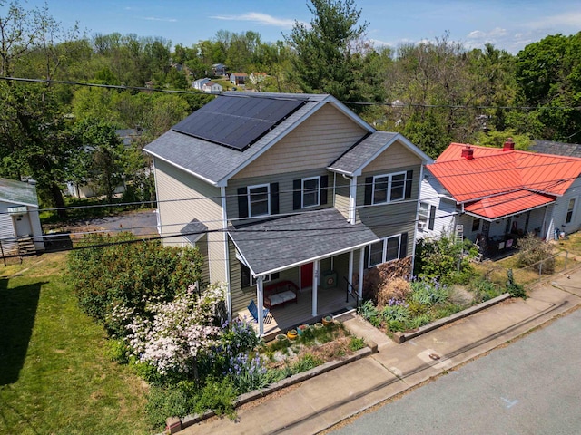 view of front of house featuring roof mounted solar panels, roof with shingles, covered porch, and fence