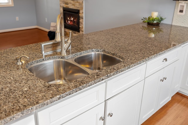 interior details with a sink, stone counters, light wood-style flooring, and white cabinetry