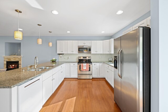 kitchen featuring light stone countertops, a sink, stainless steel appliances, white cabinetry, and a peninsula
