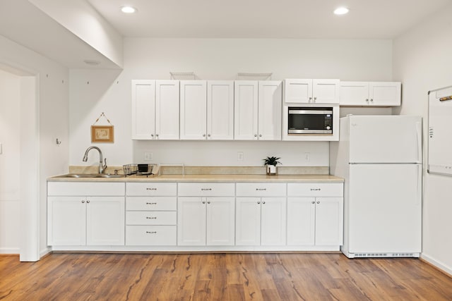kitchen featuring freestanding refrigerator, stainless steel microwave, a sink, and white cabinets