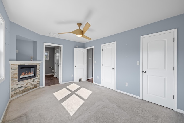 unfurnished bedroom with visible vents, a glass covered fireplace, baseboards, carpet flooring, and ensuite bath