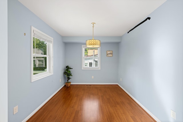 unfurnished dining area featuring plenty of natural light, baseboards, wood finished floors, and visible vents
