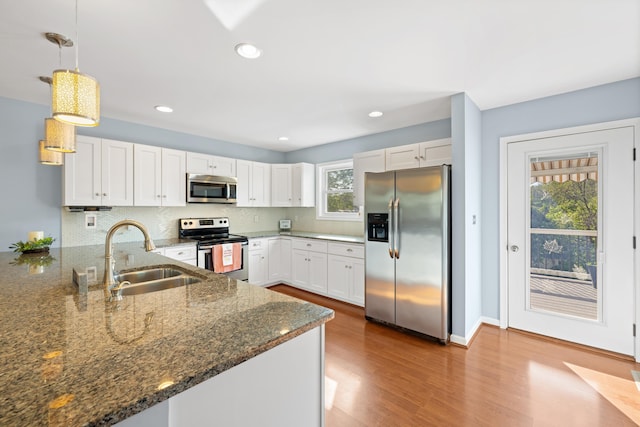 kitchen featuring a peninsula, wood finished floors, dark stone counters, a sink, and stainless steel appliances