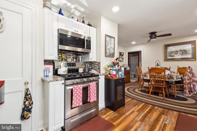 kitchen featuring hardwood / wood-style floors, decorative backsplash, white cabinets, and appliances with stainless steel finishes