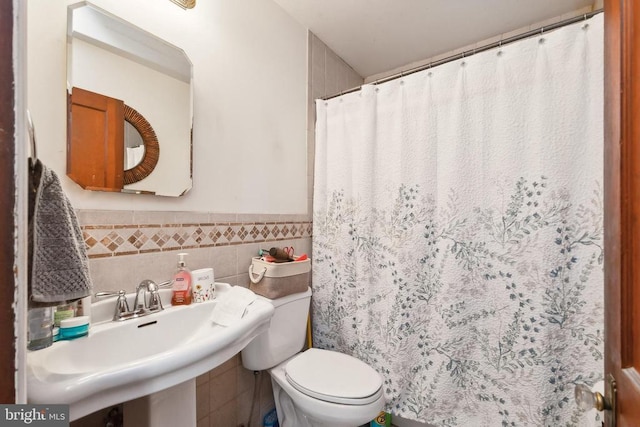 bathroom with toilet, sink, and tile walls