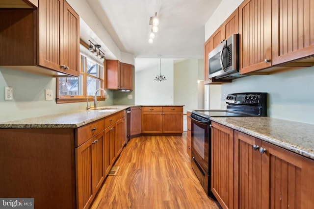 kitchen with brown cabinetry, a peninsula, stainless steel appliances, light wood-type flooring, and a sink