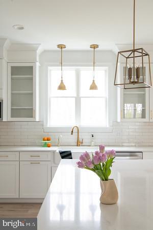 kitchen featuring pendant lighting, sink, hardwood / wood-style floors, white cabinets, and decorative backsplash