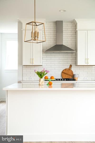 kitchen with gas stovetop, white cabinetry, decorative light fixtures, decorative backsplash, and wall chimney range hood