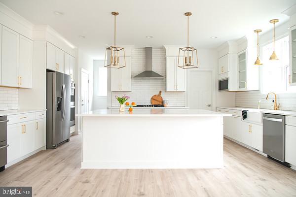 kitchen with pendant lighting, stainless steel appliances, wall chimney exhaust hood, and a kitchen island