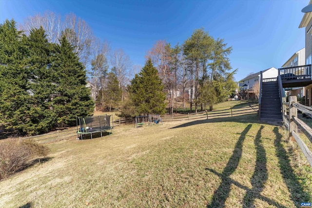 view of yard featuring stairway, a deck, a trampoline, and a fenced backyard