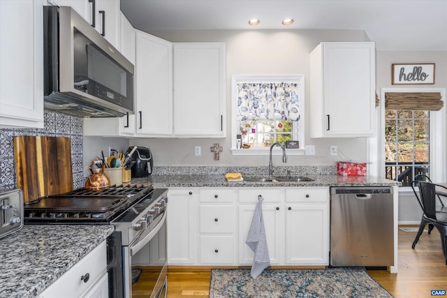 kitchen with a sink, stone counters, appliances with stainless steel finishes, and light wood finished floors