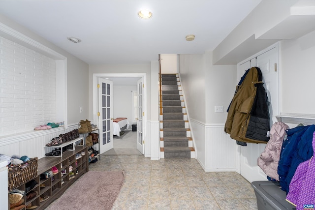 entryway featuring stairs, light tile patterned floors, french doors, and a wainscoted wall