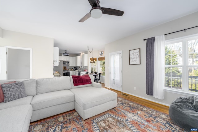 living area with baseboards, ceiling fan, and wood finished floors